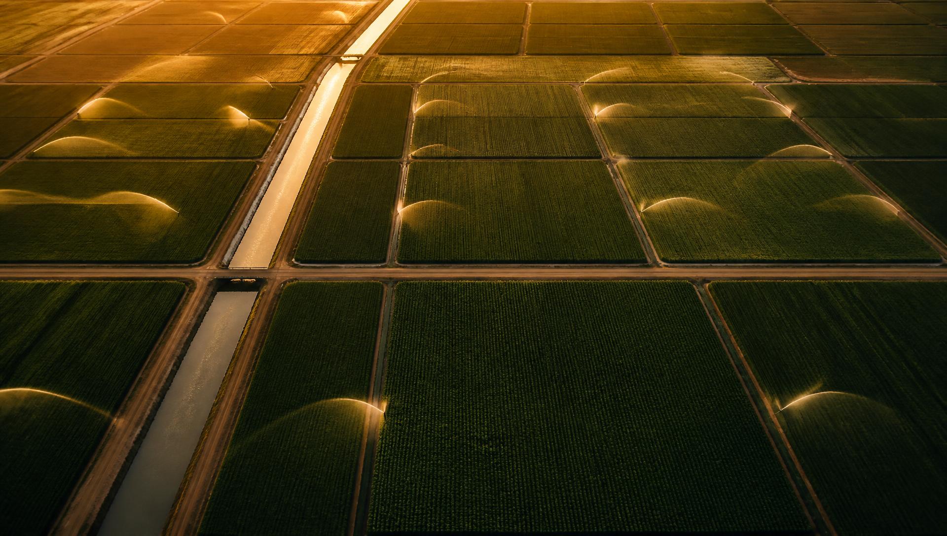 Aerial view of large irrigated farmland with sprinkler arcs and a water channel